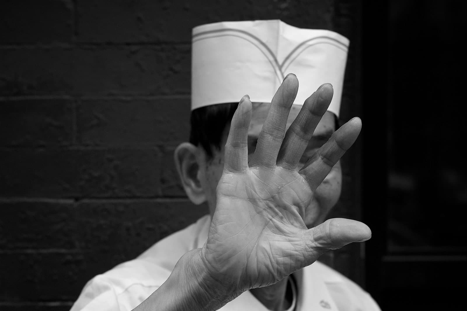 Privacy, by Thomas Leuthard. Street photo of a food service worker. He is holding his right hand in front of his face because he doesn't want to be photographed.