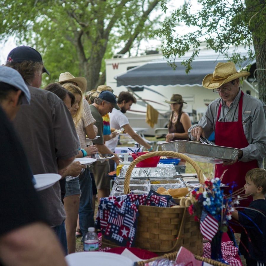 Lovin’ Spoonful Catering owner Seth Weatherford of Kerrville, Texas dishes out tasty grub to the hungry artists & crew at Woody Guthrie Folk Festival 16 while his grandson helps out.